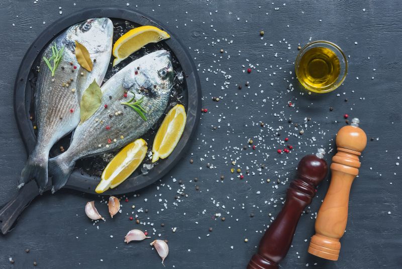 Dwie surowe ryby z cytryną i listkami świeżych ziół leżące na patelni i przygotowanie do grillowania.