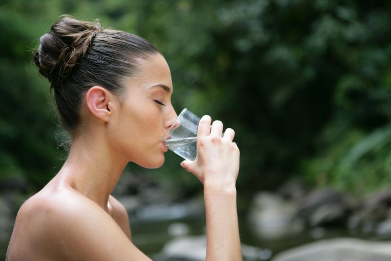 Młoda kobieta pijąca wodę ze szklanki.